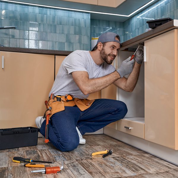 Smiling young caucasian home master working with screwdriver in kitchen, installing furniture. Home master concept, construction and repair